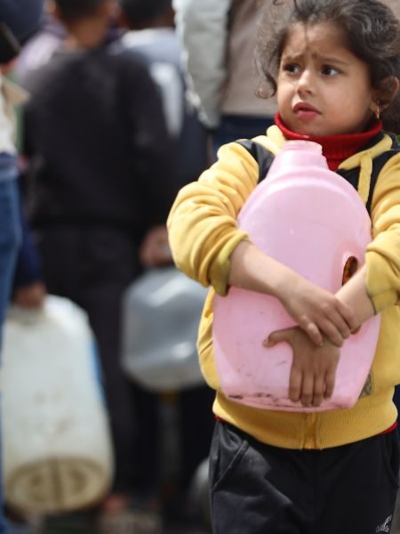 Une petite fille touchée par la guerre à Gaza tient un bidon d'eau dans ses bras