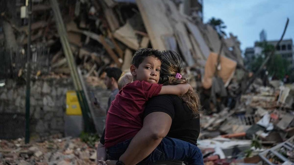 Un enfant dans les bras de sa mère marches sur les décombres d'un immeuble effondré lors du séisme survenu le 24 juin 2026 au Nord de Caracas, au Venezuela.