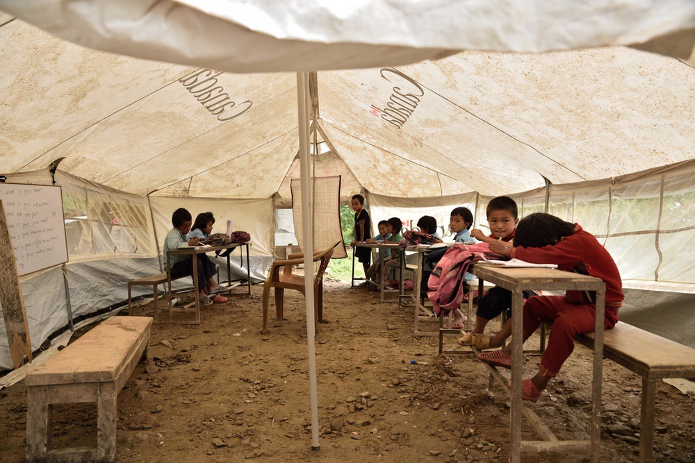 Séismes Népal - L'école primaire du village a été détruite par les séismes. Vingt enfants, de 4 à 9 ans, assistent désormais aux cours sous une toile de tente. Le village voudrait reconstruire l'école dans les semaines à venir mais n'a pas assez d'argent.